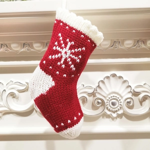 Detail of red and white knitted Christmas stocking with snowflake pattern on fireplace