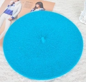 Flat lay of a sky blue wool beret hat on white lace background with a lifestyle touch