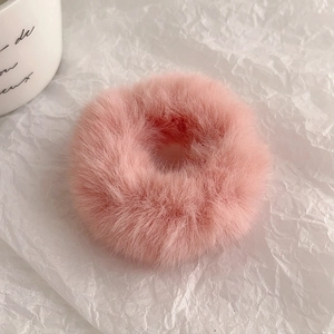 Close-up of soft pink plush hair scrunchie with fluffy texture on white textured paper