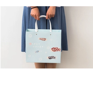 Person holding light blue paper gift bag with red carp streamers and Japanese greeting