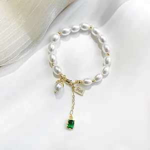Close-up of pearl bracelet with 'Faith' engraved tag and emerald gemstone pendant