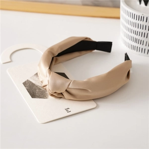 Detailed view of beige knotted satin headband with non-slip lining on a white desk