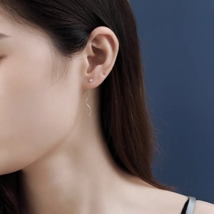 Detail of s925 silver wave tassel earrings worn by a model against a blue background