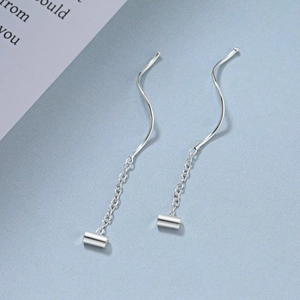 Macro shot of silver wave tassel earrings with cylindrical charms on blue texture