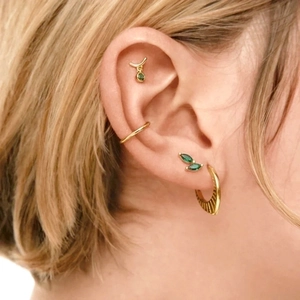 Gold earrings set with marquise green zircons and textured hoops on female ear