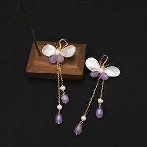 Macro shot of butterfly pearl earrings with purple tassels on a wooden display stand