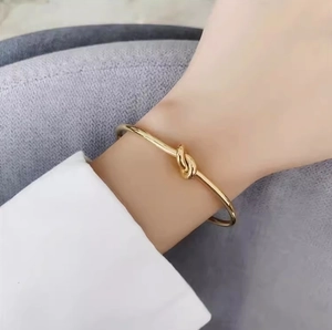 Elegant gold knot open bangle in polished stainless steel worn on a female wrist