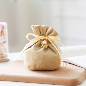 Detail of velvet wedding favor bag in champagne gold with silk ribbon and pearl charm