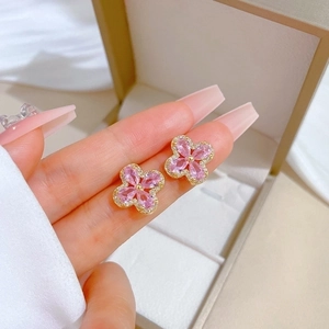 Close-up of pink four-leaf clover stud earrings with crystal halo held by hand