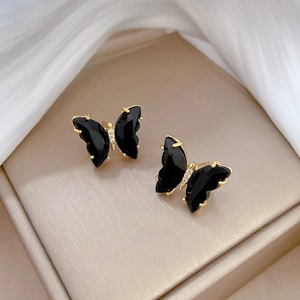 Macro detail of black crystal butterfly earrings with gold plating on satin background