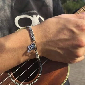 Close-up of a silver cross pendant and double chain bracelet on a man's wrist