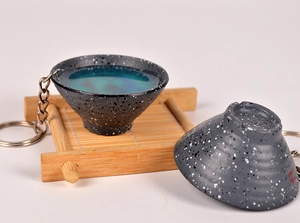Macro detail of miniature ceramic tea bowl keychains with blue resin liquid and bamboo mat