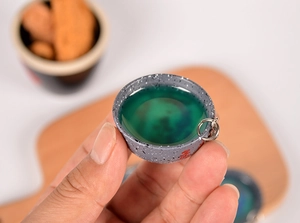 Detailed macro view of a miniature soup bowl keychain with green resin and lucky symbol