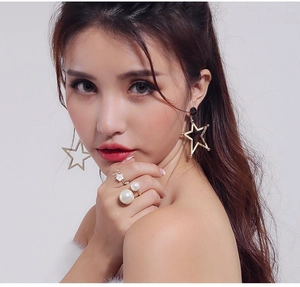 Detail of creative floral ring and large pearl ring styled with gold star earrings