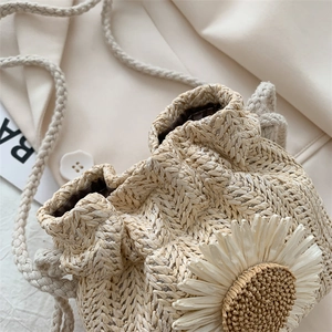 Close-up of beige woven bucket bag featuring delicate daisy detail and drawstring