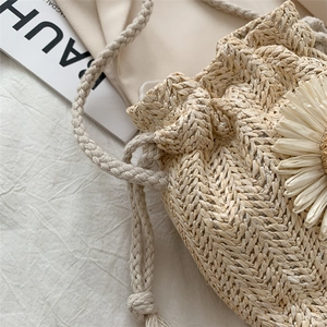 Detail view of woven straw bucket bag with large floral accent and thick rope drawstring