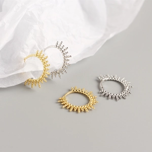 Detailed view of silver and gold spiked sunburst hoop earrings on textured background