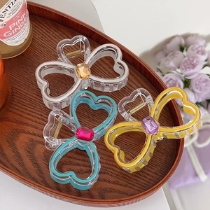 Three heart-shaped hair claws in white blue and yellow frames on a wooden tray