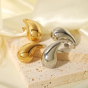 Polished 18k gold and silver teardrop earrings displayed on a luxury stone platform