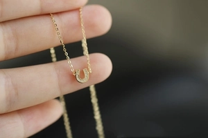 Detailed close-up of a 14K gold plated silver U-shaped horseshoe pendant with small diamonds