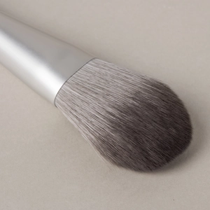 Macro shot of a flat fan-shaped makeup brush with silver metal handle and soft gray bristles
