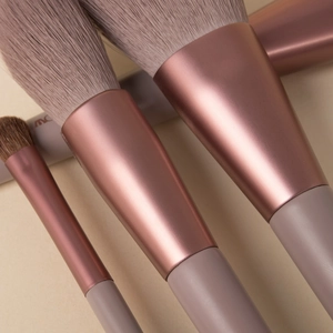 Close-up of rose gold and taupe makeup brushes on a beige textured background