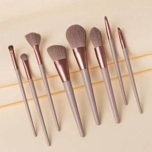 Close-up of 8 grey-purple makeup brushes with rose gold ferrules on beige fabric