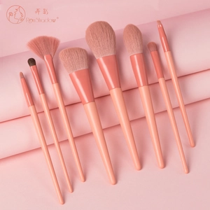 Detail of coral pink makeup brush set with soft bristles and matte handles on curved background