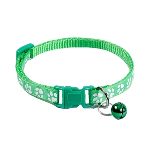 Detail view of a green pet collar with white paw prints, plastic buckle, and a bell