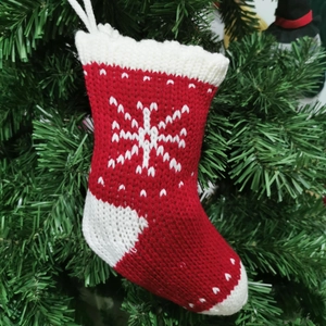 Close-up of red and white knitted Christmas stocking with snowflake pattern on green branch