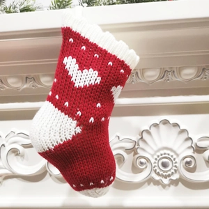 Detail of red and white knitted Christmas stocking hanging by a rustic white fireplace
