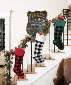 Three knitted plaid Christmas stockings in red, black, and green hung on stairs