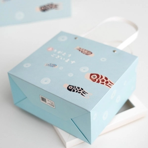 Pastel blue gift bag with Japanese koi fish design and white woven handle on white desk