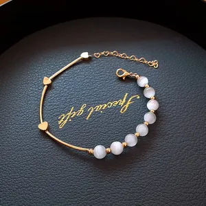 Close-up of gold-plated heart bracelet with white beads and lobster clasp on black tray