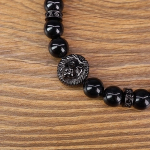 Detailed shot of black beaded bracelet with lion head charm on wooden surface