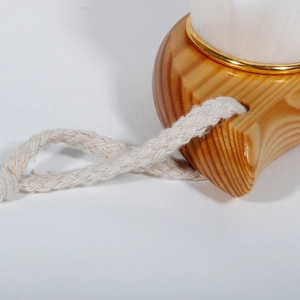 Detail of wooden facial cleansing brush with soft white bristles and a cotton hanging rope
