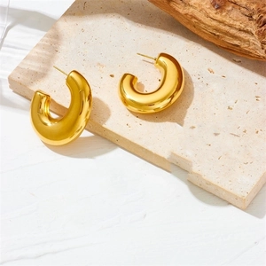 Detail of high-polished gold hollow C-shaped hoop earrings on a beige travertine stone
