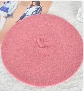 Top-down view of a pink wool beret hat laid flat on a white lace background