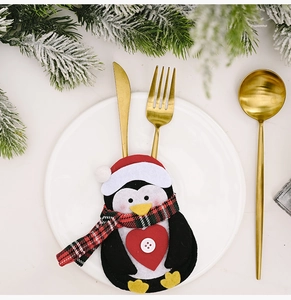 Close-up of penguin-shaped Christmas cutlery holder on a white plate with pine branches