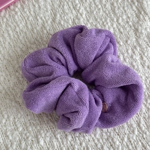 Close-up of a purple towel fabric hair scrunchie with a round metal tag on white knit