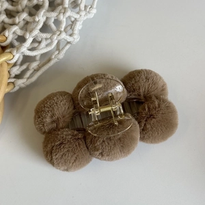 Detail shot of brown plush faux fur pom-poms on a transparent claw clip with gold spring