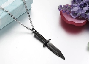 Macro detail of a black dagger pendant on a silver steel chain next to a gift box