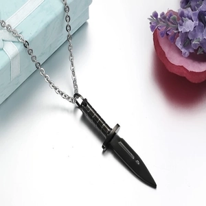 Macro shot of a black dagger pendant on a silver steel chain next to a white gift box