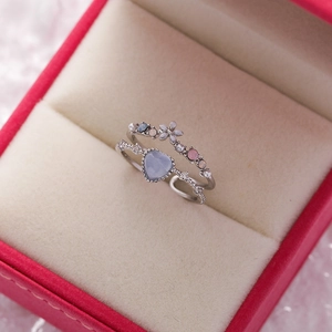 Detailed view of heart-shaped blue gem and floral wave rings in a pink jewelry box
