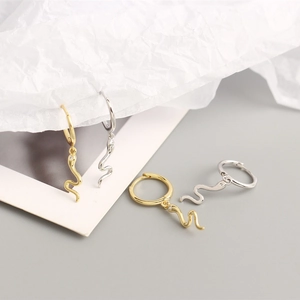Detail of gold and silver snake hoop earrings with small gemstone accents on paper