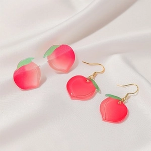 Detail of pink gradient peach earrings with green leaves on white silk background