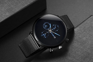 Close-up of black quartz watch with Milanese strap and three-eye decorative dial.