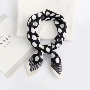 Classic black and white polka dot silk square scarf tied in a bow on a soft knit surface
