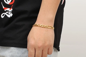 Detailed close-up of a gold-plated Figaro chain bracelet on a male model's wrist
