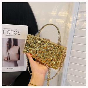 Detailed shot of golden acrylic box bag featuring unique metal texture and curved handle